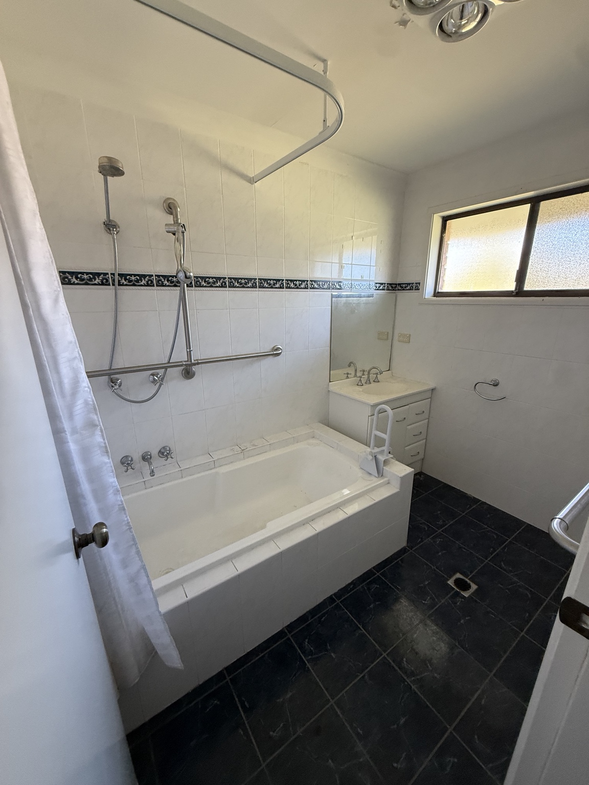 Our original bathroom with a built-in bath, shower curtain, white wall tiles and dark floor tiles